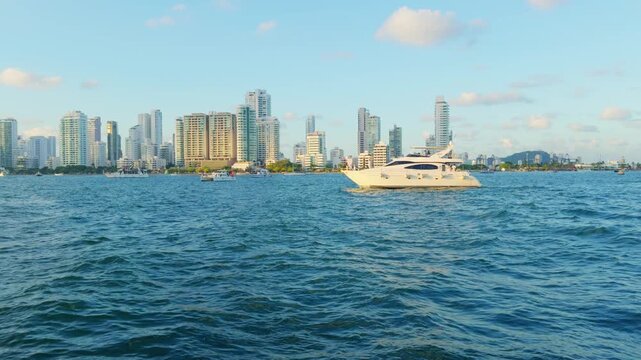 Luxury yacht cruising off Cartagena Colombia, Caribbean waterfront skyline, modern towers and coastal architecture, sparkling blue sea, sunny tropical atmosphere, premium travel and tourism experience