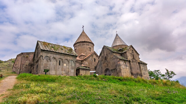 Historic Armenian Goshavanq Monastery ruins on grassy hillside under cloudy skies