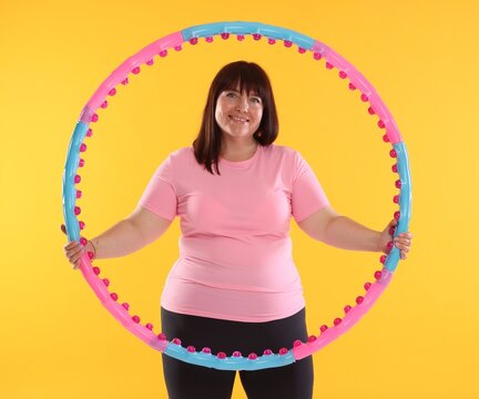 Overweight woman with hula hoop on orange background. Sports equipment