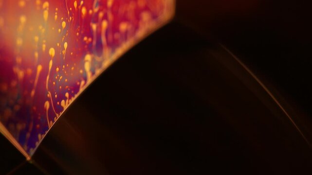 Glowing golden fluid plane with rising plume tendrils and dark red background. Warm golden and fiery orange backlighting illuminates a diagonal fluid film plane in low-key macro perspecti