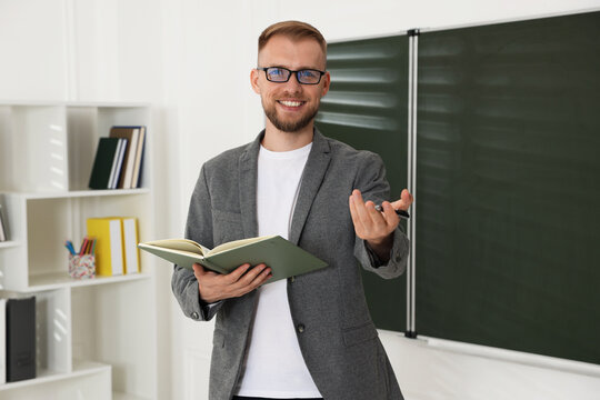 Portrait of smiling teacher in glasses and suit with book conducting lesson in classroom