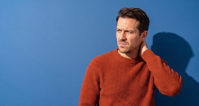 Man looking thoughtful while touching his neck against blue background  