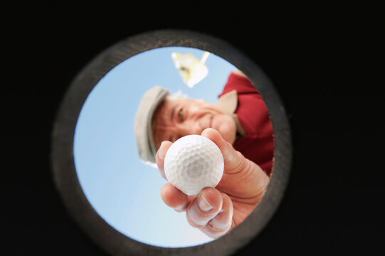 Man retrieves golf ball from the hole outdoors