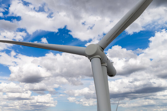 Aerial view of a wind turbine blade and hub set against a bright blue sky with scattered white clouds in the United Kingdom.