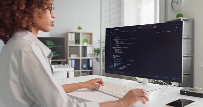 Programmer developer woman coding at computer office. She focuses on code at a monitor, hands on keyboard, delivering reliable software in a modern IT workplace. Clear concept of coding teamwork.
