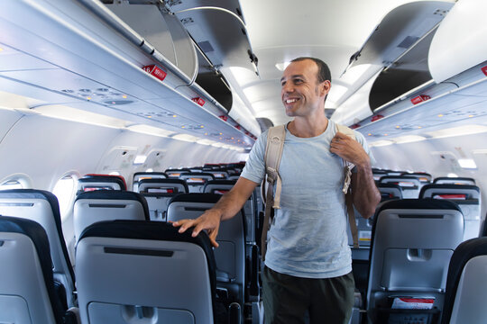 Smiling man with backpack standing in empty airplane cabin aisle