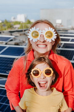 Smiling mother and daughter wear flower sunglasses by solar panels