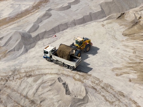 Aerial view of a yellow wheel loader filling a dump truck with gravel in a large quarry in the United Kingdom.