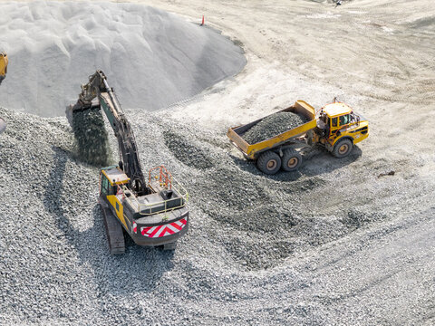 Aerial view of an excavator loading gravel into a yellow dump truck at a quarry in the United Kingdom.