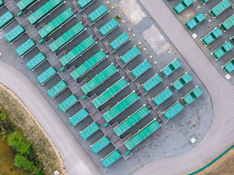 Aerial view of rows of green shipping containers or modular units arranged on a gravel lot with paved walkways in the United Kingdom.