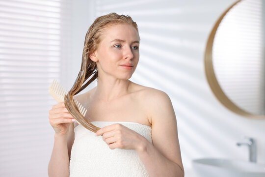 Woman brushing hair after applying mask in bathroom
