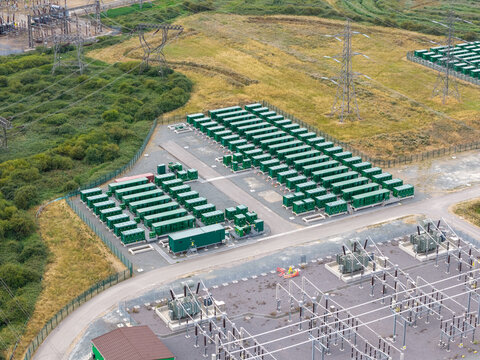 Aerial view of a battery energy storage system facility with rows of green containers and electrical infrastructure in the United Kingdom.