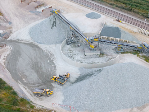 Aerial view of a gravel processing facility with conveyor belts, large piles of crushed stone, and yellow dump trucks operating in the United Kingdom.