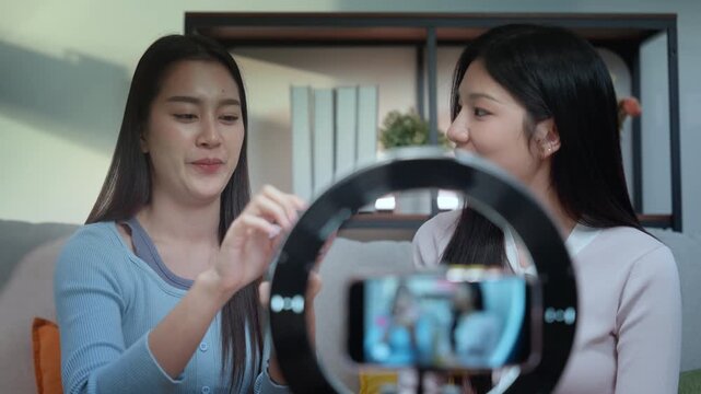 Beauty bloggers influencers live streaming makeup tutorial vlog with smartphone and ring light at home studio, two young women share skincare and makeup on camera, warm focus and smile