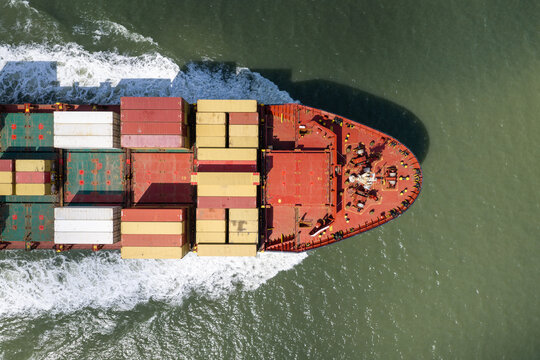Aerial view of a large cargo ship loaded with colorful shipping containers moving through the sea in the United Kingdom.