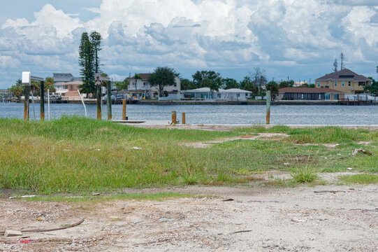 Calm bayfront scene with grassy shoreline, wooden docks and waterfront homes framed by dramatic summer clouds, conveying peaceful coastal living, leisure boating potential and suburban seaside atmosph