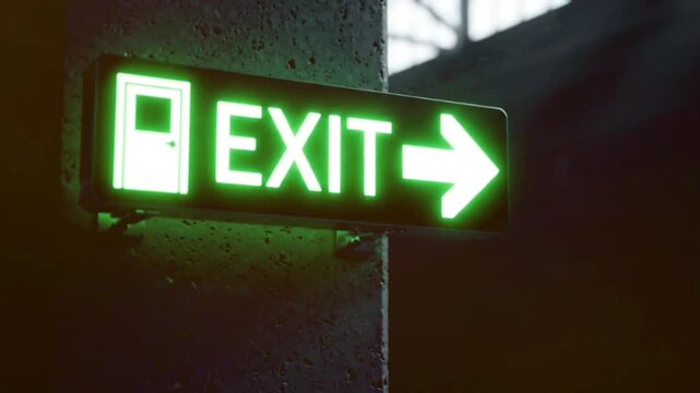 Green glowing rectangular light sign indicating emergency exit mounted on grey textured concrete wall in dark industrial corridor environment cinematic footage.