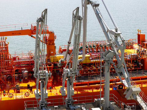 Aerial view of an industrial oil tanker deck featuring mechanical loading arms, orange painted surfaces, and complex piping systems on the sea in the United Kingdom.