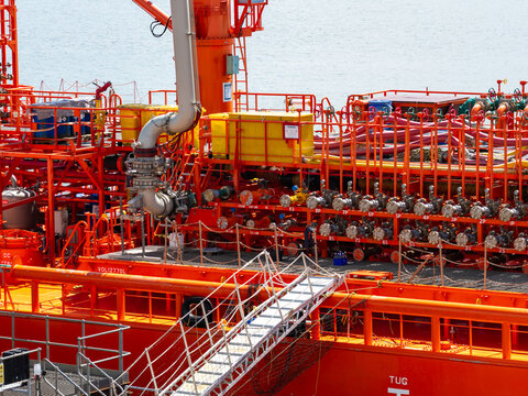 Aerial view of the industrial deck of an oil tanker featuring bright orange piping, complex valve systems, and metal walkways in the United Kingdom.