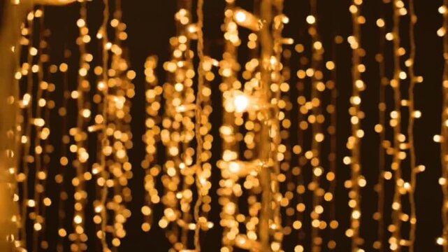 Strings of golden led fairy lights hanging vertically against dark background create warm festive ambiance with bokeh effect and soft cinematic camera motion.