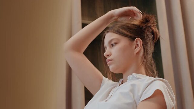 Young woman styling hair in mirror, poised grooming session with soft lighting, expressive motion and modern aesthetic, preparation for day with editorial vibe and effortless confidence.