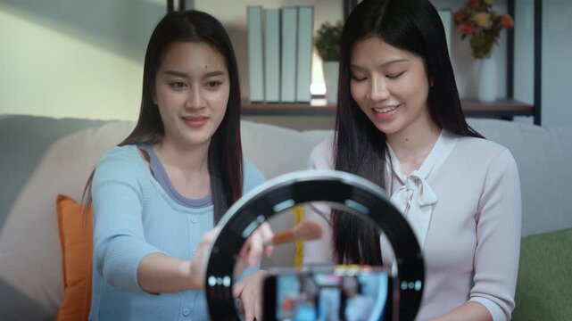 Beauty blogger influencer live streaming makeup tutorial with expert lighting and smartphone tips, brush techniques, two Asian women in home studio sharing natural blush guide for followers