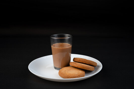 Traditional Indian tea in a clear glass and Biscuit isolated on a black background