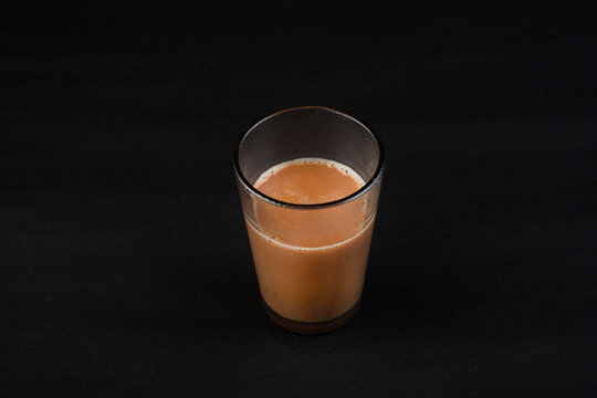 Traditional Indian frothy tea in a clear glass isolated on a black background