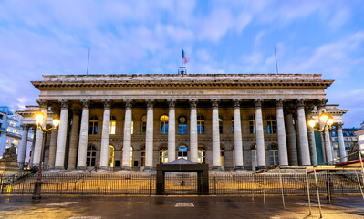 Fototapeta premium Illuminated facade and neoclassical columns of Palais Brongniart, the historic stock exchange building in Paris, France at dusk.