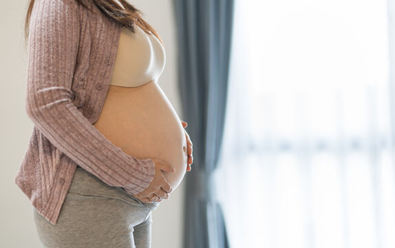 Side view close-up of a pregnant woman holding her belly with both hands.