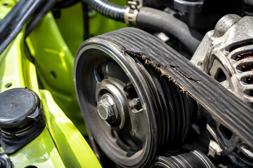 Fototapeta premium Damaged serpentine belt with frayed edges runs across engine pulleys, showing severe wear that requires automotive maintenance.