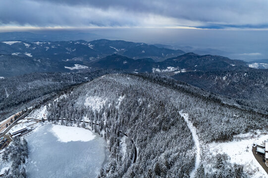Aerial view of the frozen Mummelsee lake surrounded by snow-covered pine forests and winding roads in the Black Forest mountains in Seebach, Baden-Wurttemberg, Germany.