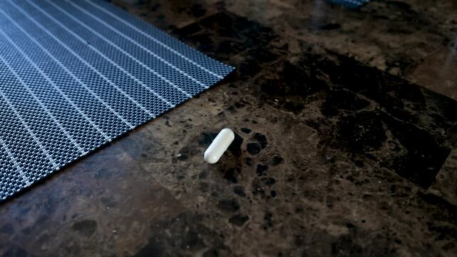 Person taking two white capsule pills from a dark marble kitchen countertop