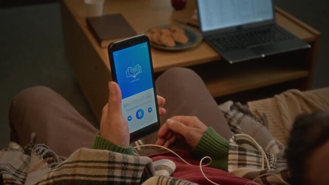 Unrecognizable man listening to audiobook on smartphone while lying down, rear view. Footage is suitable for marketing digital education platforms and mobile learning apps