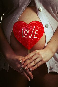 A pregnant woman holds a large red heart-shaped lollipop