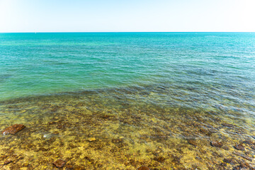 Fototapeta premium Clear turquoise sea water over rocky seabed near shoreline with transparent shallow water revealing underwater stones, concept of summer vacation and nature
