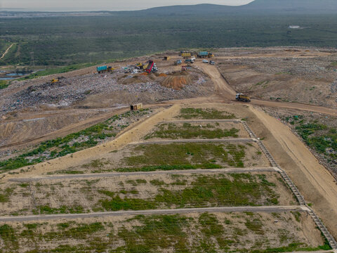 Aerial view of the Vissershok Road landfill site with heavy machinery and dump trucks operating on waste piles amidst dirt roads in Cape Town, Western Cape, South Africa.