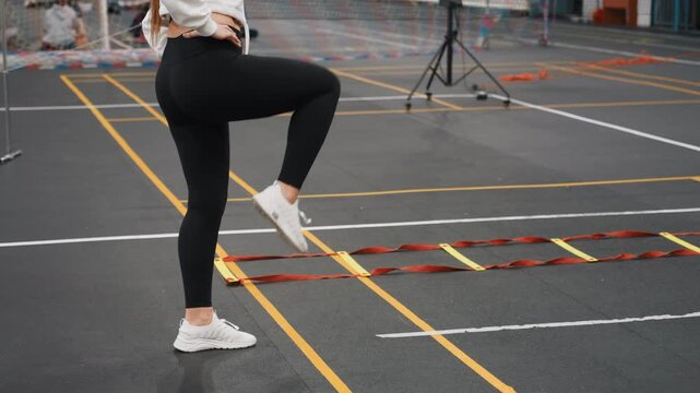 Badminton court ladder drill demo white female athlete showcasing polished footwork, confident singleleg lifts and measured pacing on indoor marked court with audience and camera setup, instructional