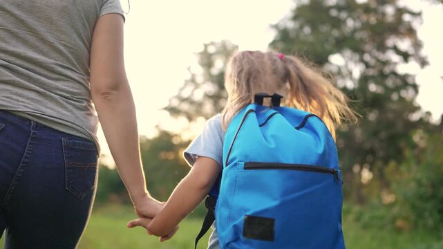 Woman holding the hand of a child. Back, school, mom, daughter go, park, backpack, schoolgirl. A schoolgirl is going to the park with her backpack. The photo is of a young girl holding lifestyle her.