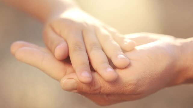 A close up image of a person holding another person's hand. Hands, mom, child, close up arms, family, park, sunset. Family in arms at sunset in the park. The photo lifestyle is of a child holding the.