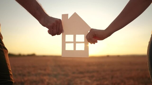 Man and woman holding paper house. Paper, house, hands, family, park, couple, hold, home,. Couple holding a baby in a park at their home. The photo is of a couple holding hands lifestyle in a field.