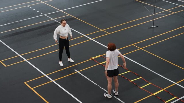 Court badminton footwork practice session, coach demonstrating ladder steps while junior athlete observes and repeats, concentrated technical training, clear court markings and net support visible