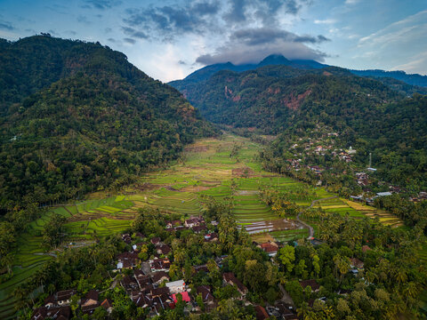 Aerial view of Kayuwangi rice terraces surrounded by lush green mountains and a small village in Banyubiru, Central Java, Indonesia.