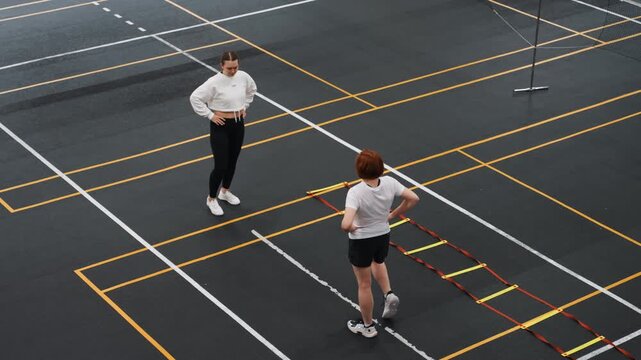 Badminton court trainer guiding precision footwork, measured technique session with athlete practicing controlled steps on agility ladder for posture, balance and mobility in indoor training clinic