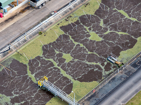 Aerial view of the solar powered waste water treatment plant featuring aeration tanks with dark sludge and green algae, metal walkways, and roads in Byron Bay, New South Wales, Australia.