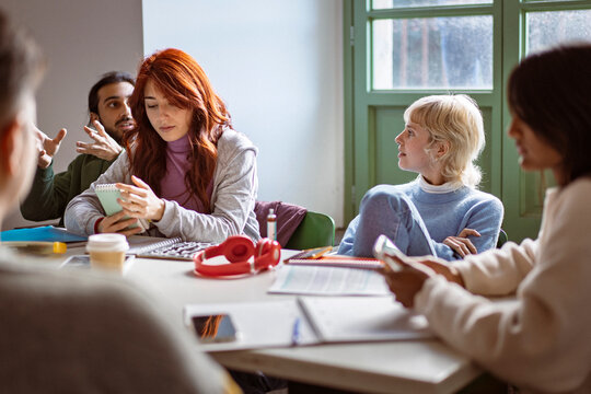 University students attending class while one student distracted by smartphone during group discussion