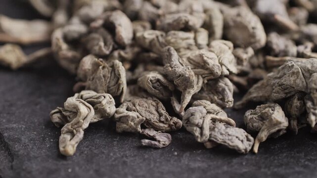 Green dried gunpowder chinese tea leaves with scoop on white wooden background, closeup.