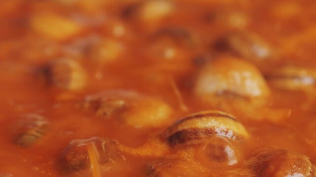 French snails, Close up of traditional spanish tapas - the boiled snails in tomato sauce with garlic and chili in black iron pan