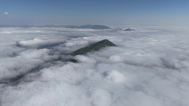 Aerial view of a mountain peak rising above a sea of clouds․