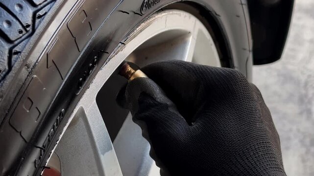 Close Up Of Gloved Hand Checking Tire Air Pressure And Screwing Valve Cap On Car Wheel